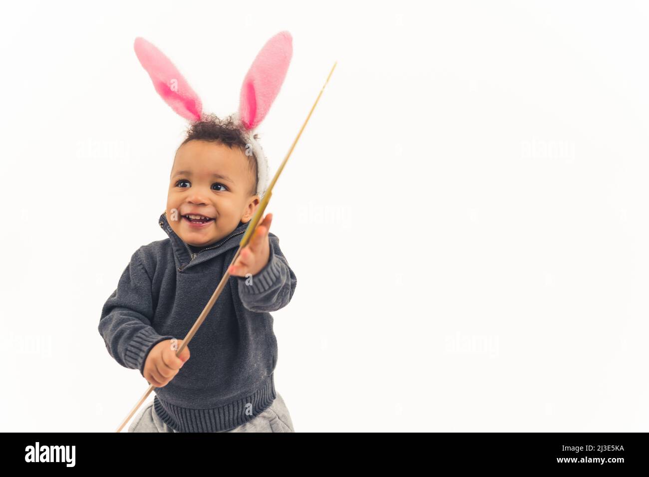 Joyeux petit garçon afro-américain avec des oreilles de lapin lauthing regardant quelque part et tenant un studio de bâton de bambou tourné fond blanc moyen espace de copie. Photo de haute qualité Banque D'Images
