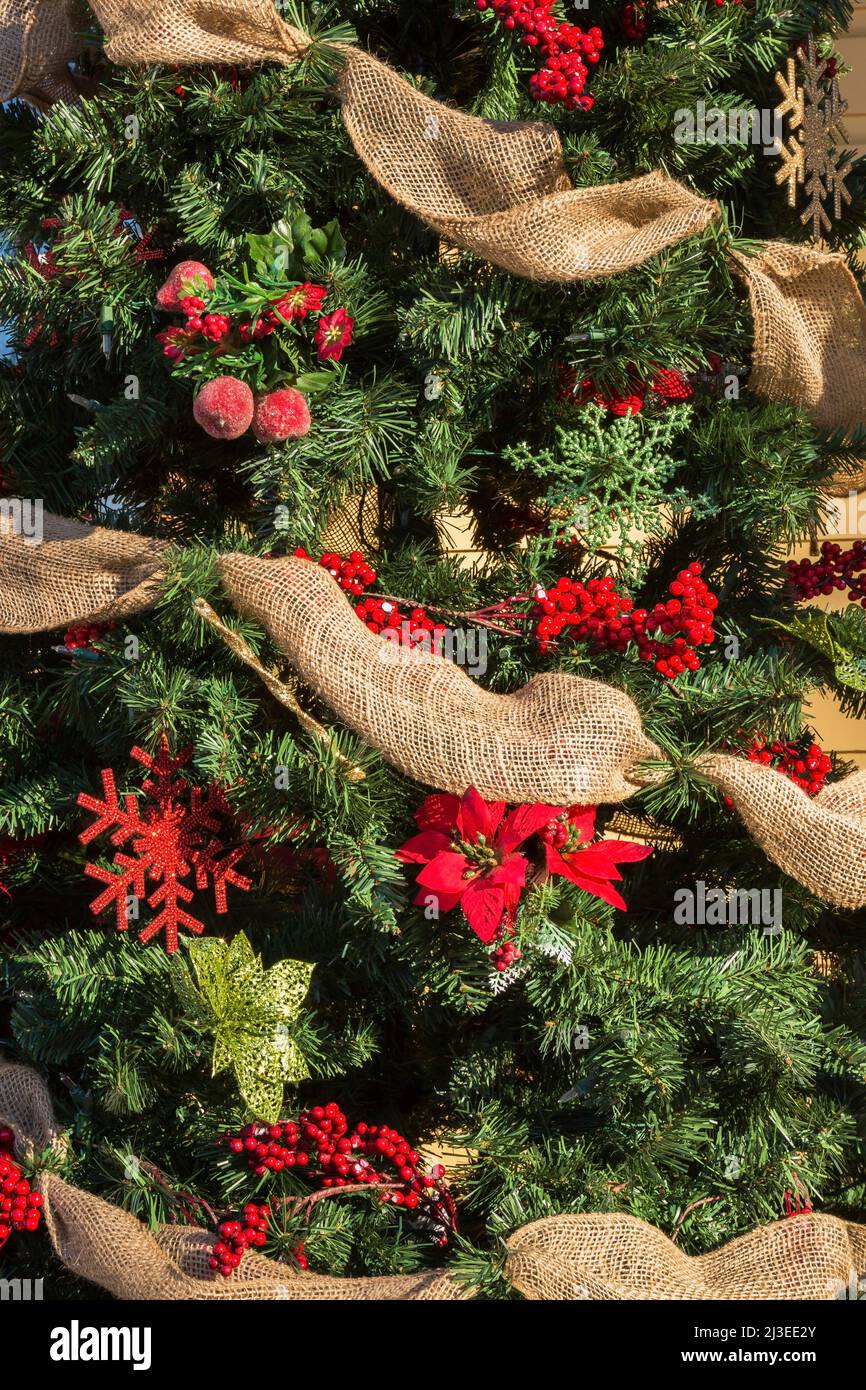 Sapin de Noël artificiel décoré de guirlandes en toile de jute, ornements rouges et verts. Banque D'Images