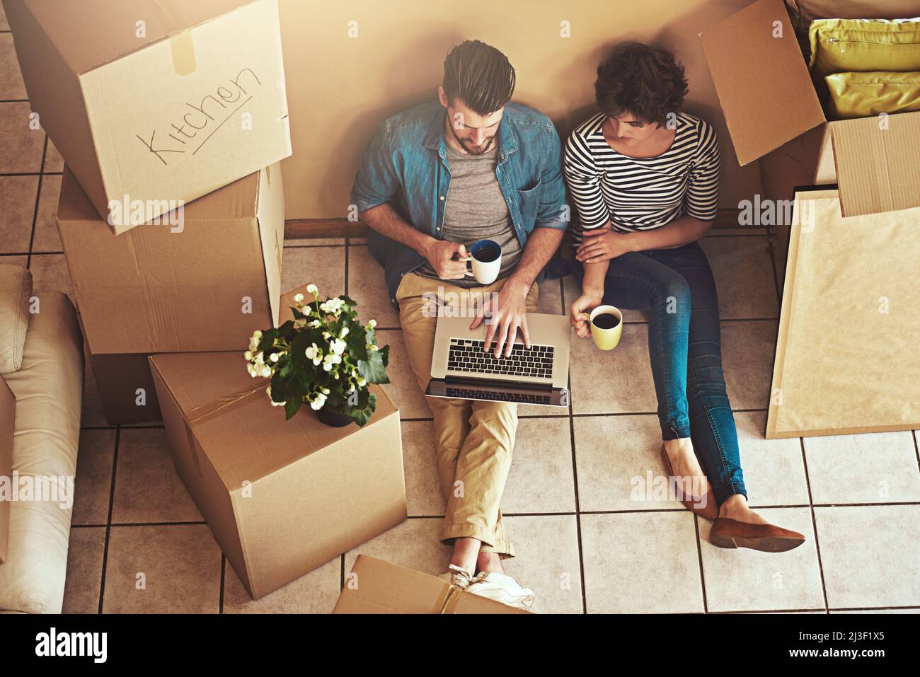 Recherche d'inspiration pour la décoration. Photo d'un jeune couple se reposant sur le sol et utilisant un ordinateur portable dans sa nouvelle maison. Banque D'Images