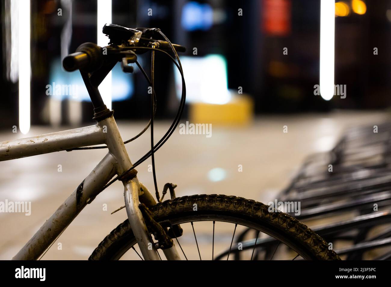 Vieux vélo de montagne sale utilisé pour les déplacements garés dans le rack de vélo au centre-ville. Photo prise le soir, lumière médiocre venant de la rue Banque D'Images