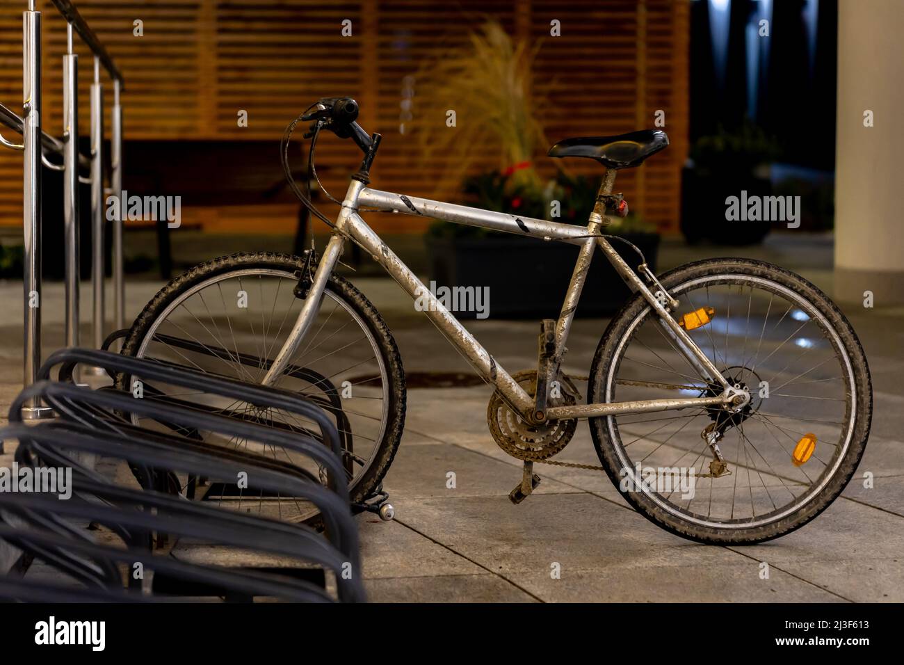 Vieux vélo de montagne sale utilisé pour les déplacements garés dans le rack de vélo au centre-ville. Photo prise le soir, lumière médiocre venant de la rue Banque D'Images