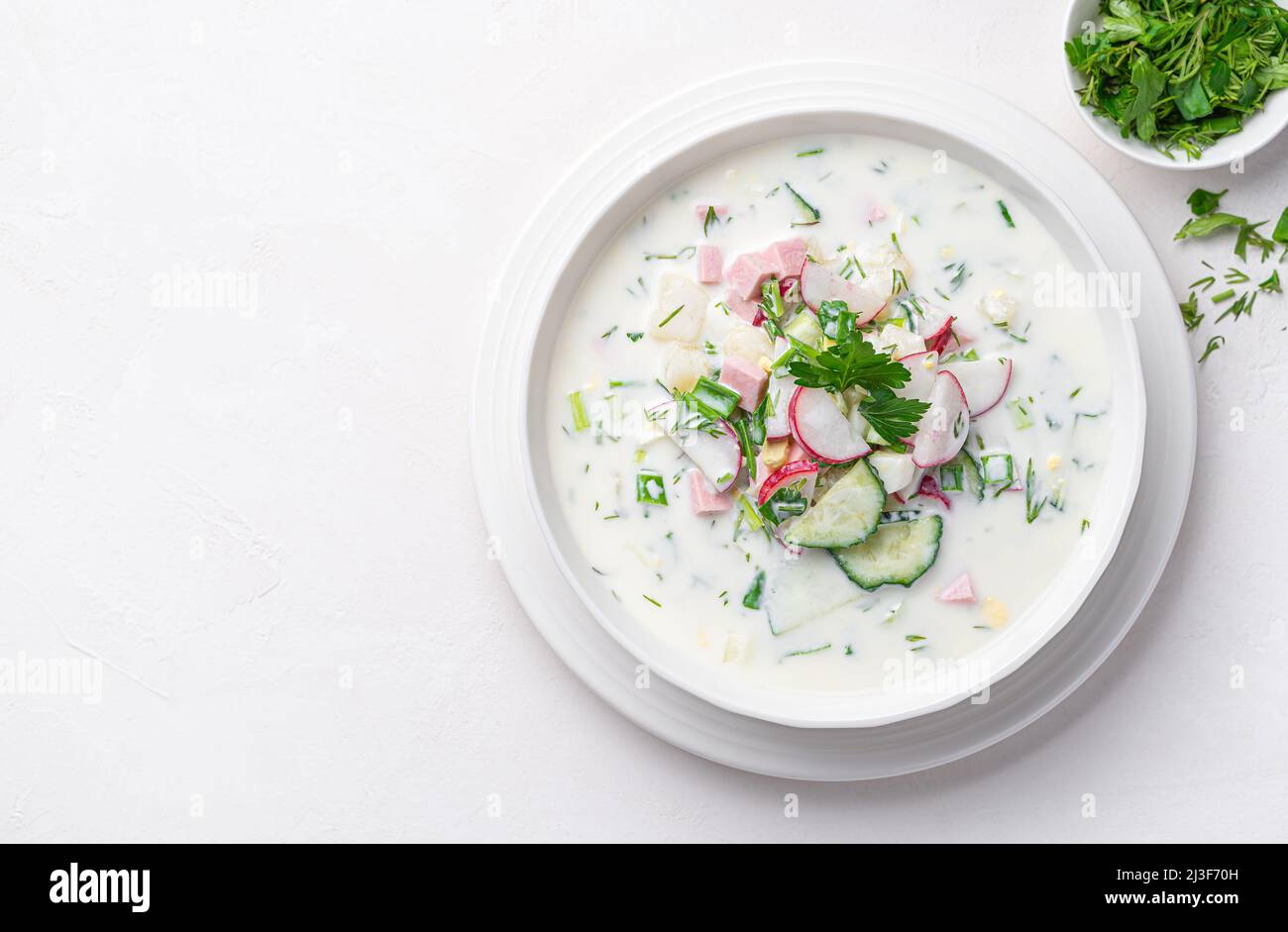 Soupe froide d'été à l'okroshka avec légumes, saucisses, herbes et kéfir sur fond blanc. Vue de dessus, espace de copie. Banque D'Images