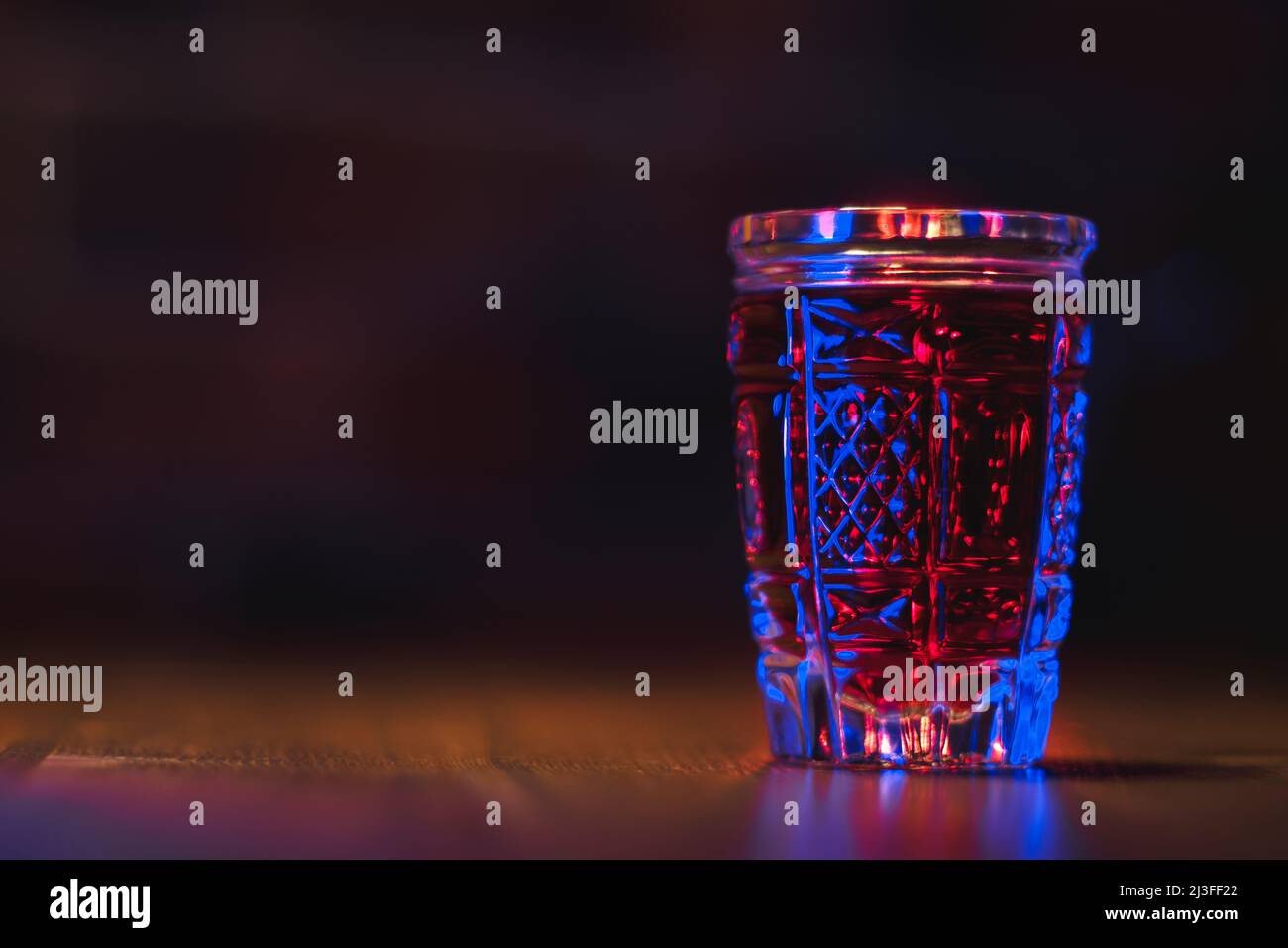 Teinture de couleur rouge dans un verre de cristal se dresse sur une table en bois dans un éclairage bleu Banque D'Images