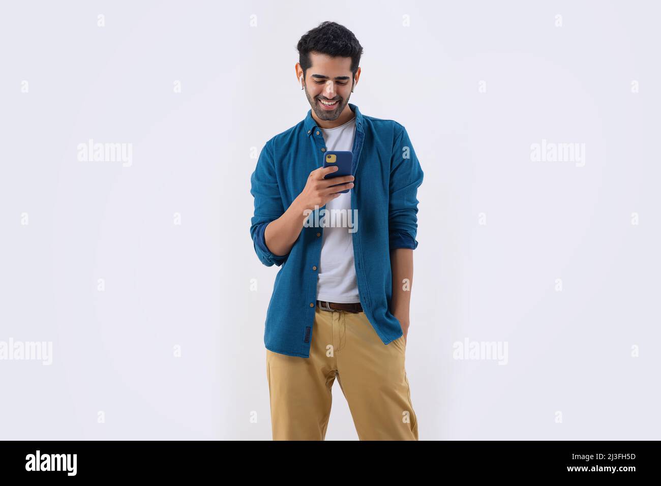 Jeune homme écoutant de la musique à l'aide d'écouteurs et mobile avec la main dans la poche Banque D'Images