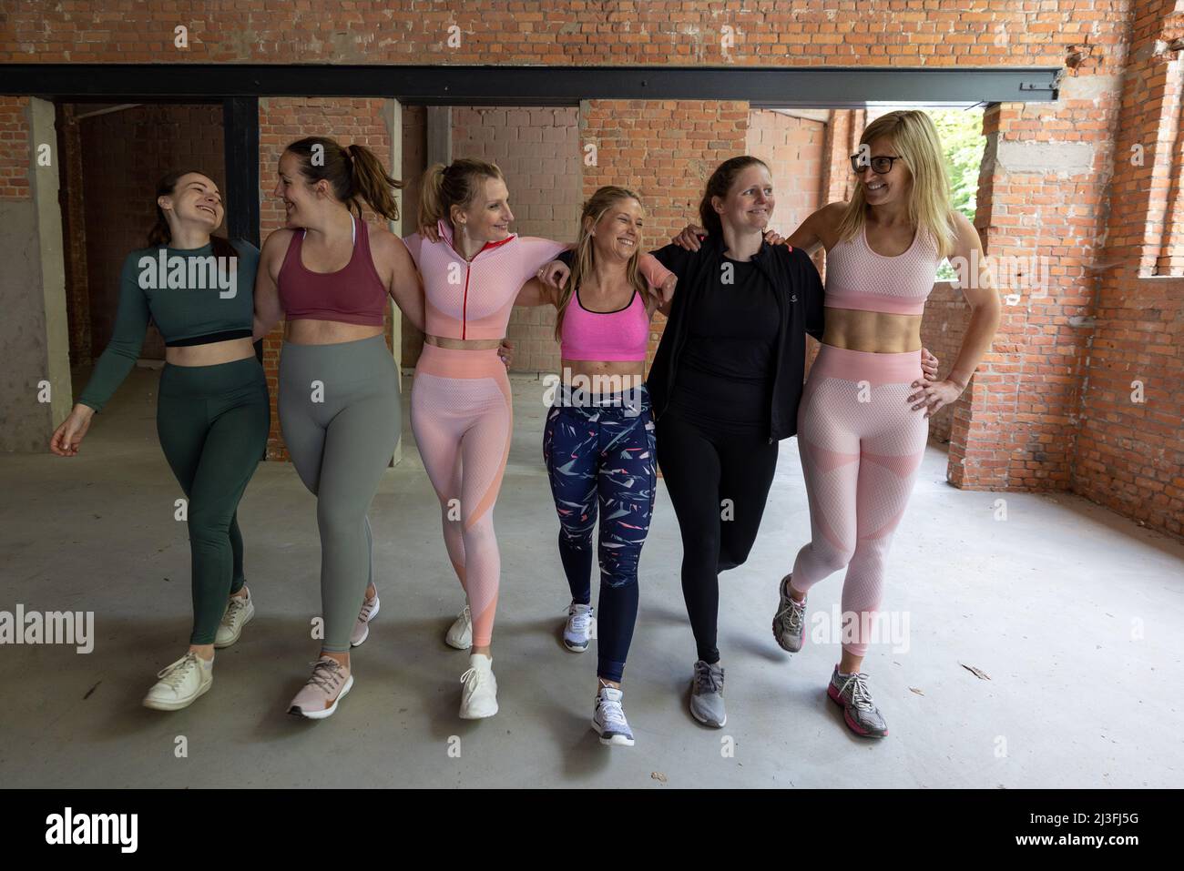 Groupe souriant d'amis de sexe féminin de divers types de corps dans les vêtements de sport bras de marche dans le bras ensemble après un cours d'entraînement dans une salle de sport. Photo de haute qualité Banque D'Images