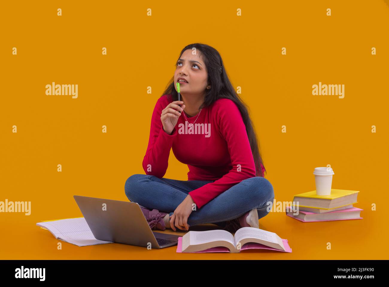 Jeune femme regardant vers le haut et pensant tout en étudiant avec un ordinateur portable et des livres Banque D'Images
