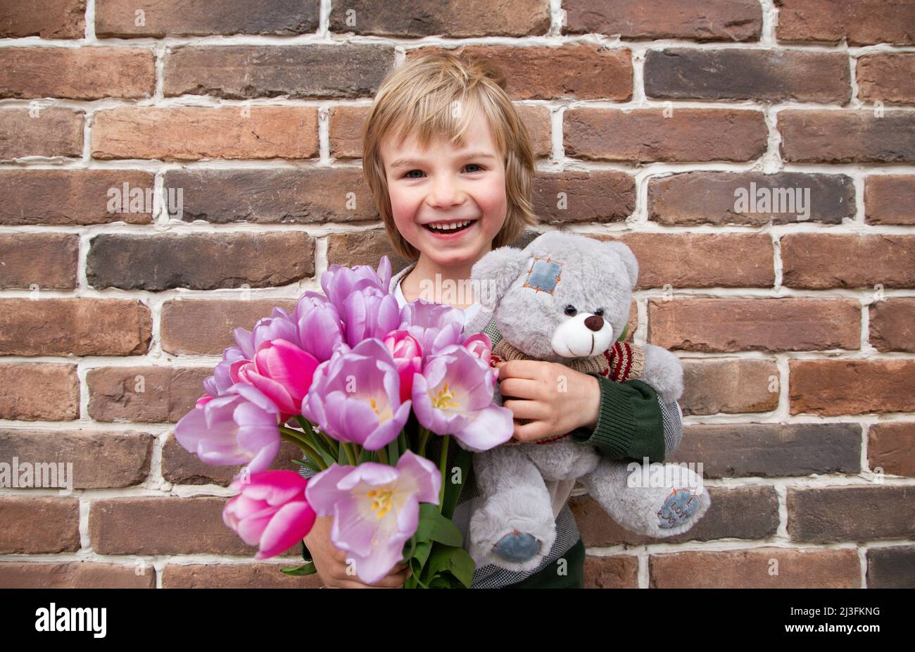 Joyeux garçon de 5-6 ans avec des fleurs de tulipe et un ours en peluche. Sourire, un cadeau avec amour. Félicitations pour la fête de la mère, la Saint-Valentin. Banque D'Images