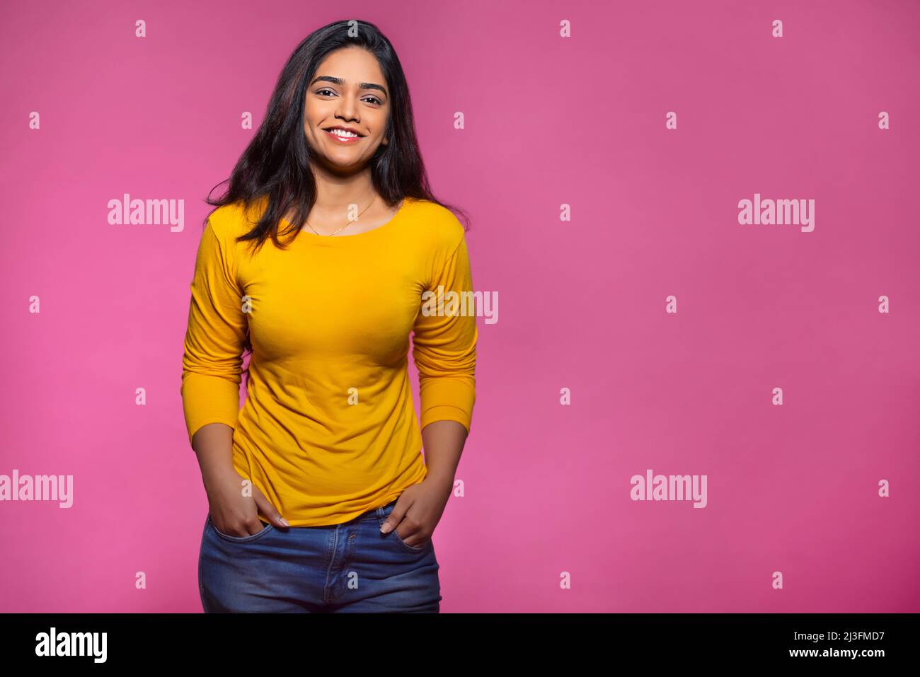 Femme adulte vêtue de couleur jaune et placée devant l'appareil photo avec les deux mains dans les poches Banque D'Images