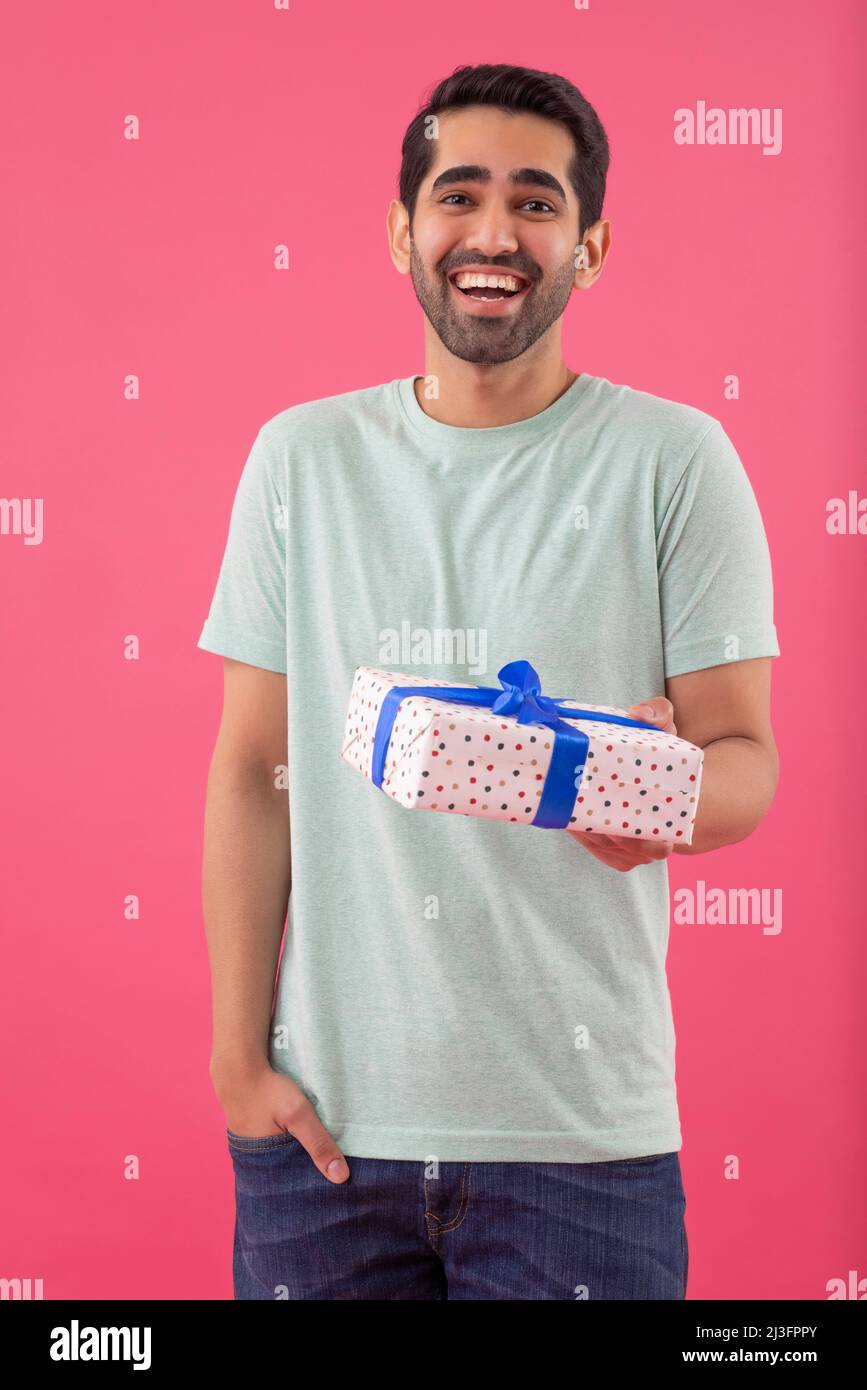 Portrait d'un jeune homme joyeux debout avec cadeau et main dans la poche Banque D'Images