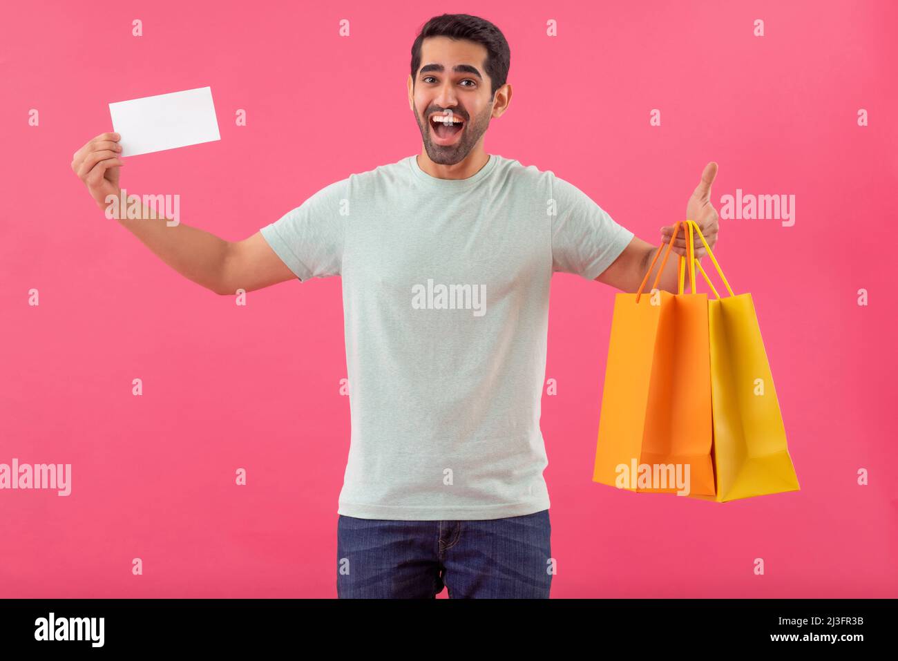 Joyeux jeune homme avec des sacs d'achats et un bon de réduction en mains Banque D'Images