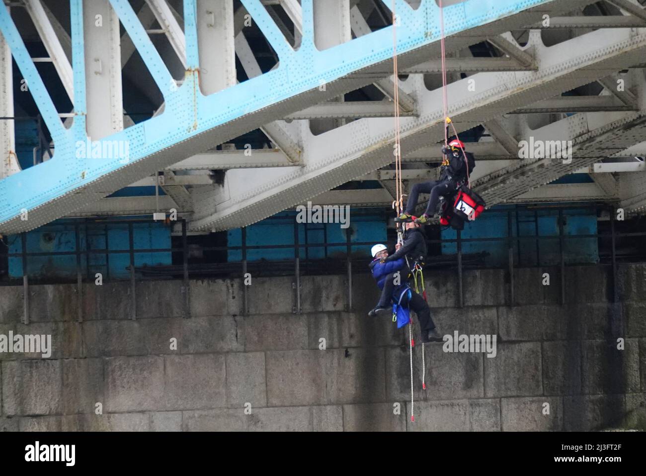 Un activiste de la rébellion d'extinction est descendu dans un bateau de police après avoir suspendu des cordes de suspension à côté d'une bannière géante qui dit « End Fossil fuels now », lors d'une manifestation sur Tower Bridge, dans l'est de Londres, qui a été fermé à la circulation. Date de la photo: Vendredi 8 avril 2022. Banque D'Images