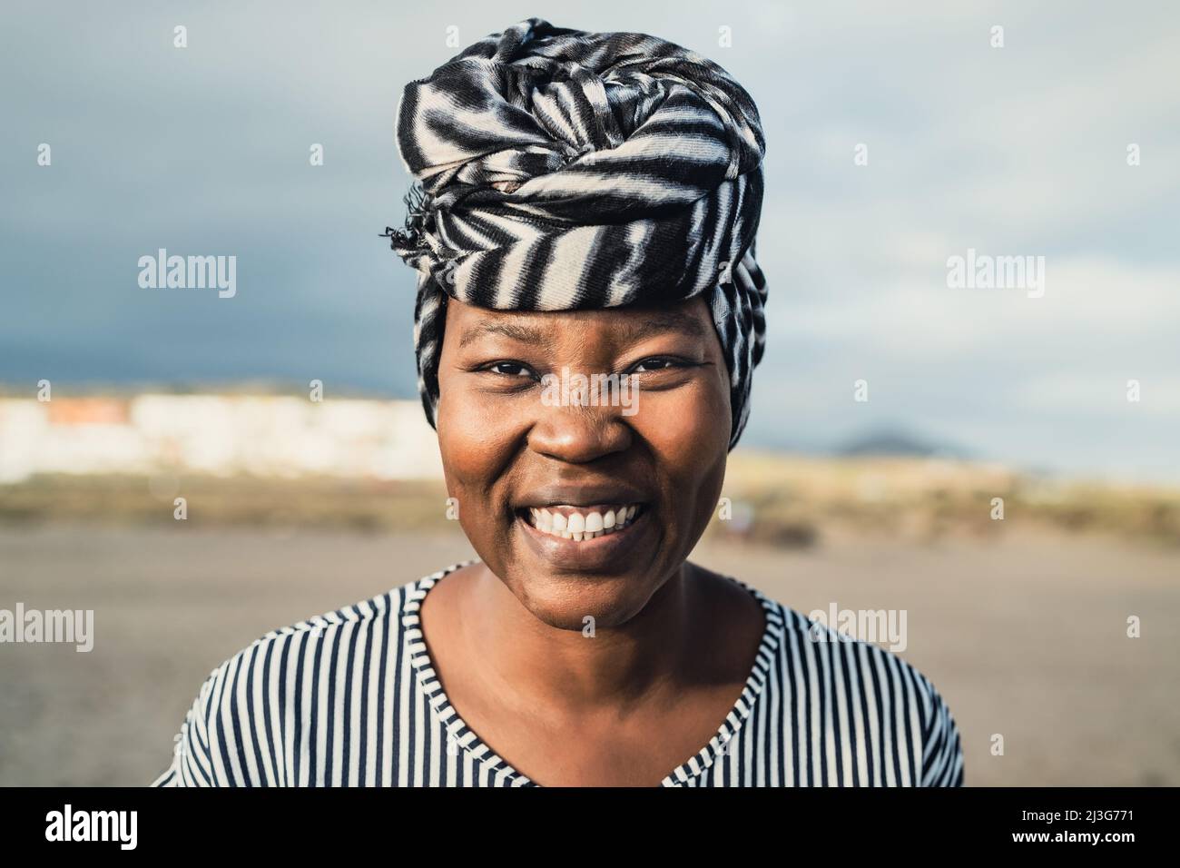 Bonne femme musulmane africaine portant le turban souriant à la caméra sur la plage pendant les vacances d'été Banque D'Images