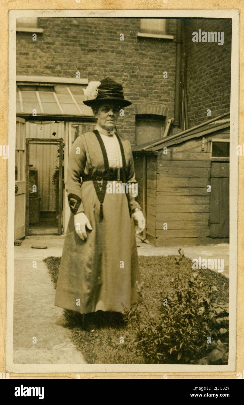 Carte de cabinet originale de l'époque édouardienne, femme âgée qui a l'air d'une poupe, peut-être une tante ou une grand-mère, portant un chapeau avec une plume et des gants blancs, à l'extérieur de sa maison urbaine dans le jardin, Crouch End, Nord. Londres, Royaume-Uni vers 1905. Banque D'Images