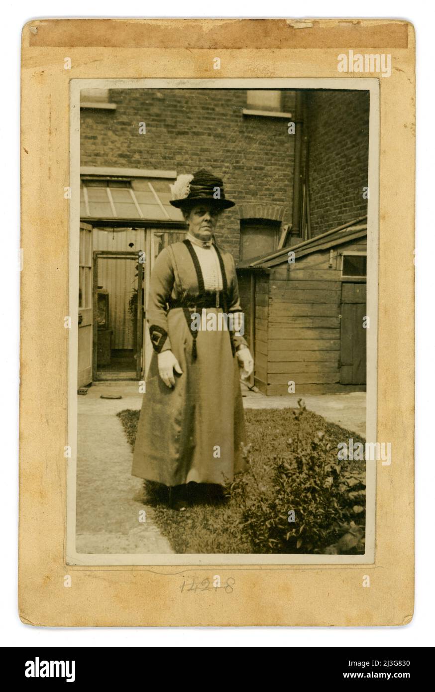 Carte de cabinet originale de l'époque édouardienne, femme âgée qui a l'air d'une poupe, peut-être une tante ou une grand-mère, portant un chapeau avec une plume et des gants blancs, à l'extérieur de sa maison urbaine dans le jardin, Crouch End, Nord. Londres, Royaume-Uni vers 1905. Banque D'Images