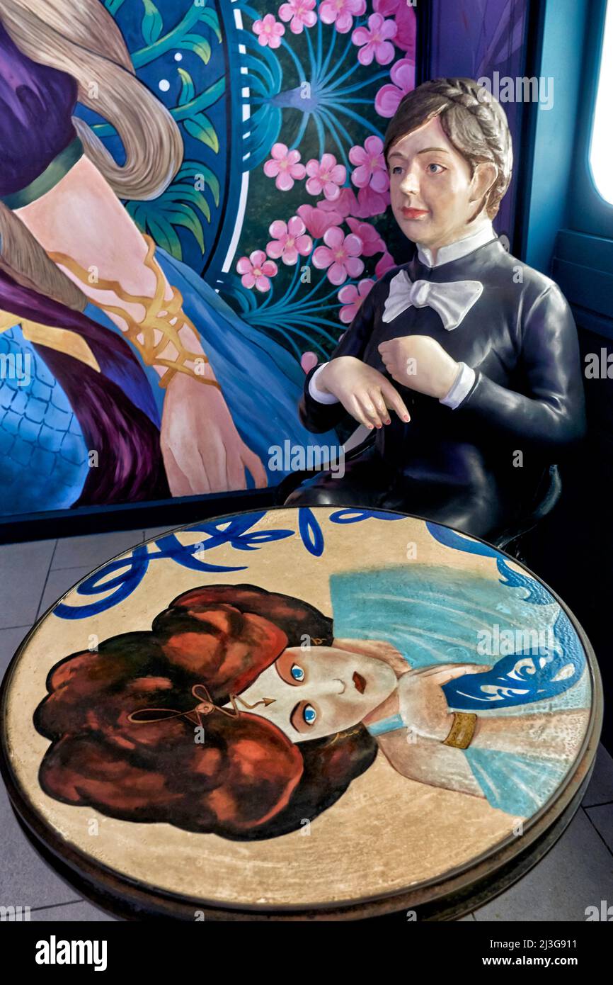 Concept de femme envie. Statue d'une femme unie assise à une table, regardant un magnifique portrait de femme peint et pensant « comment l'autre moitié vit ». Banque D'Images