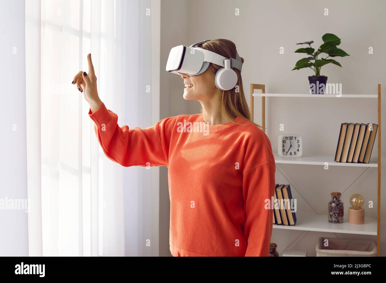 Femme heureuse portant un micro-casque VR innovant, expérimente la réalité virtuelle et joue à des jeux Banque D'Images