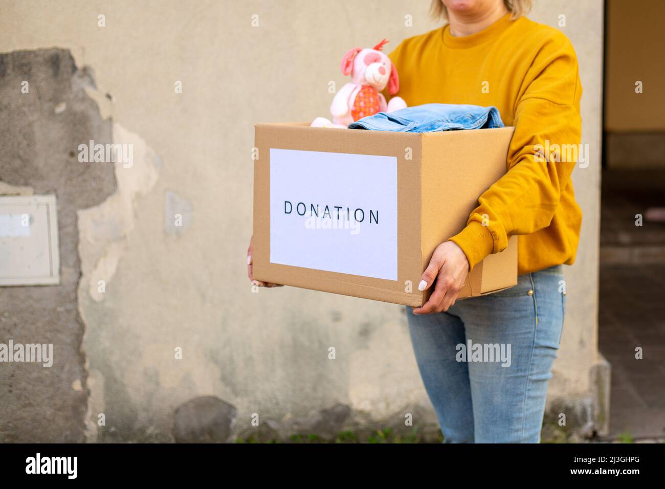 Une volontaire femelle tient une boîte d'aide humanitaire avec des choses et des jouets pour enfants pour les besoins des Ukrainiens dans la rue. Aide pour l'Ukraine Banque D'Images