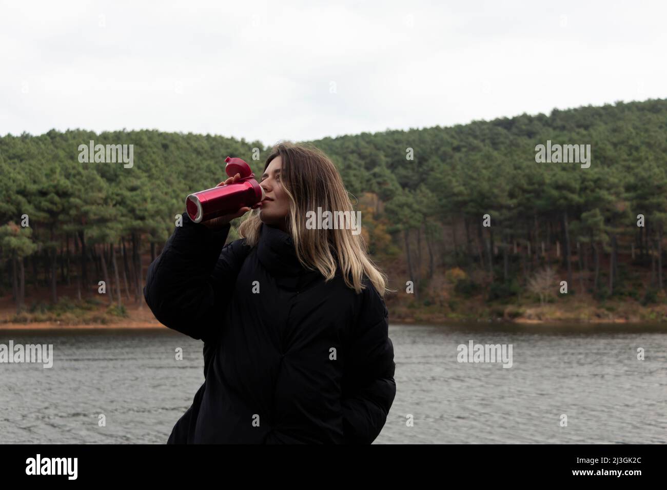 Jeune fille blonde se reposer et boire des boissons chaudes de ses thermos dans un parc naturel le jour de l'automne doré. Elle . Lac, arrière-plan en bord de mer. Banque D'Images