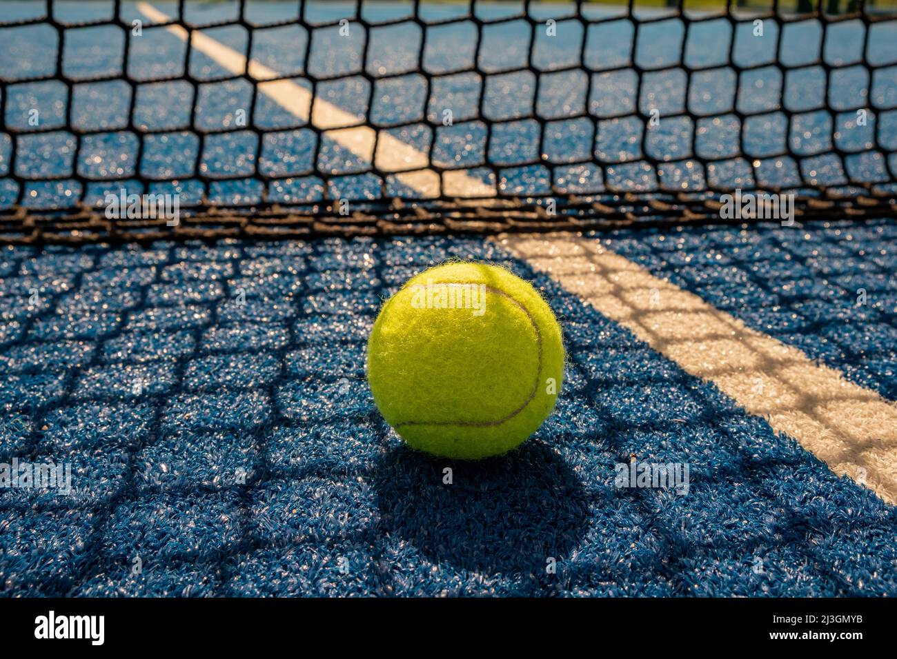 une paddle-tennis avec l'ombre du filet d'un court de paddle-tennis bleu au coucher du soleil, concept de sports de raquette Banque D'Images