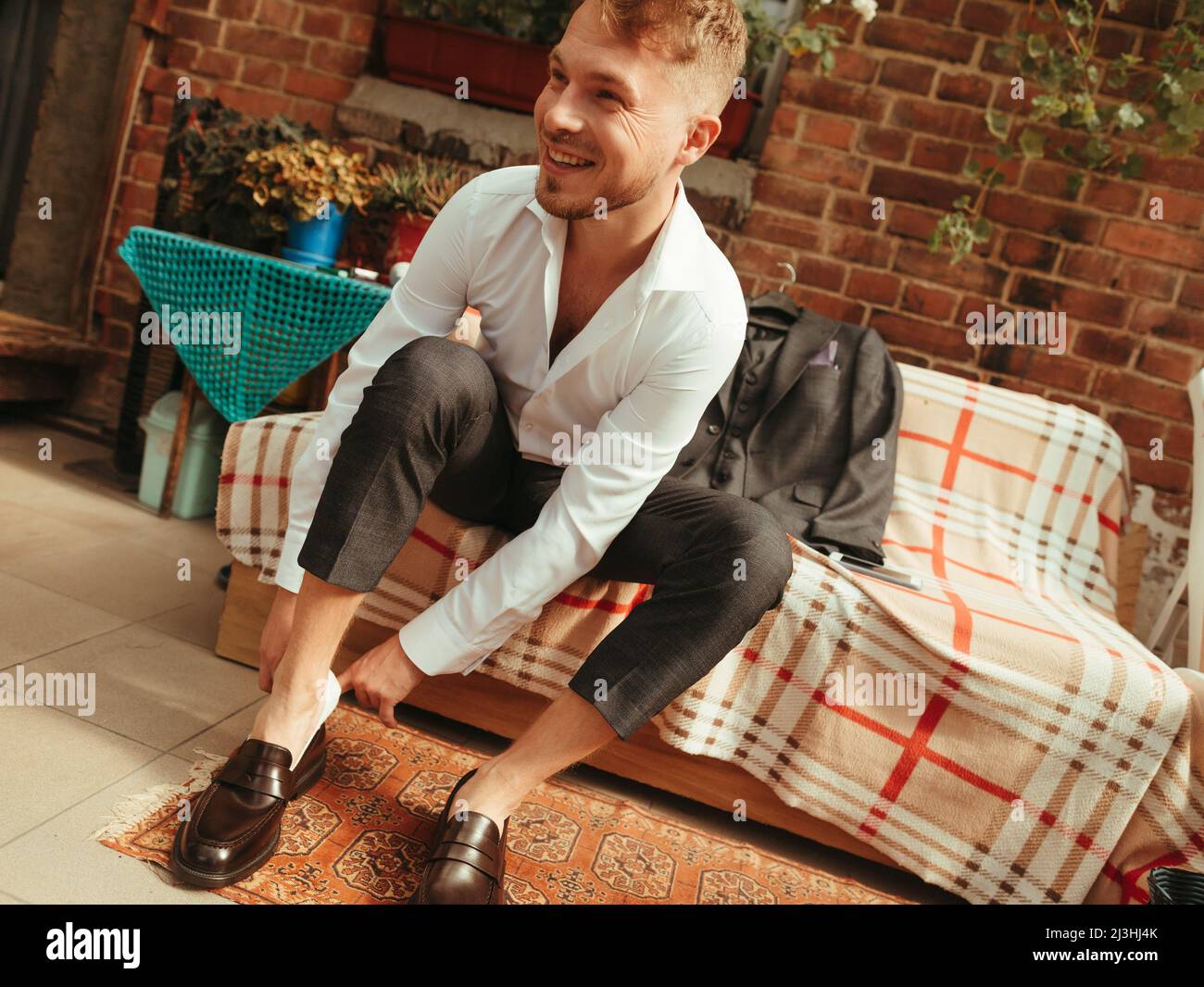 L'homme a ses chaussures élégantes dans sa chambre. Jeune homme d'affaires élégant assis sur le lit dans la chambre d'hôtel et portant ses chaussures élégantes. Effet grain Banque D'Images
