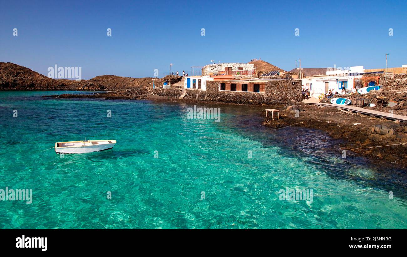 Espagne, îles Canaries, Fuerteventura, voyage en voilier, île de Los Lobos, réserve naturelle, site d'atterrissage, bâtiment, petit bateau flottant sur de l'eau verte cristalline, bleu ciel et sans nuages Banque D'Images