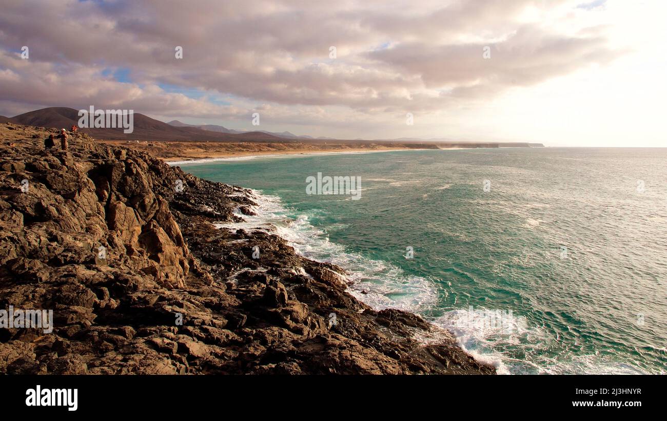 Espagne, îles Canaries, Fuerteventura, côte ouest, plage au sud de Punta de Toston, côte rocheuse sauvage, surf fort, vert de mer, ciel nuageux, début du coucher du soleil Banque D'Images