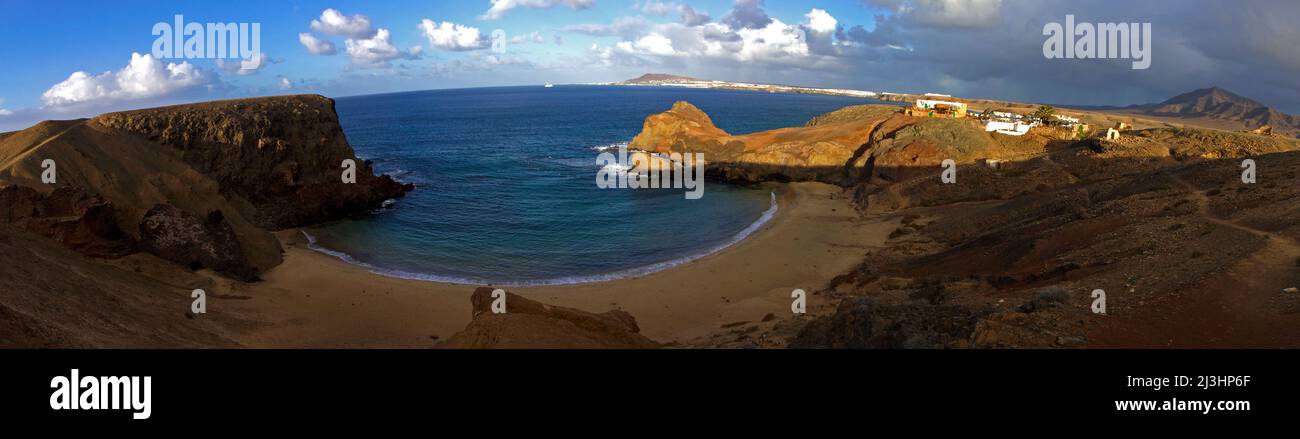 Îles Canaries, Lanzarote, île volcanique, ambiance après-orage, plages de Papagallo, Désert, bleu ciel avec nuages gris-blanc, lumière du matin, panorama à 180° depuis le dessus de la plage, rochers d'un côté baignés par la lumière du matin, bâtiments à la lumière du matin, mer ouverte et littoral de Lanzarote en arrière-plan Banque D'Images