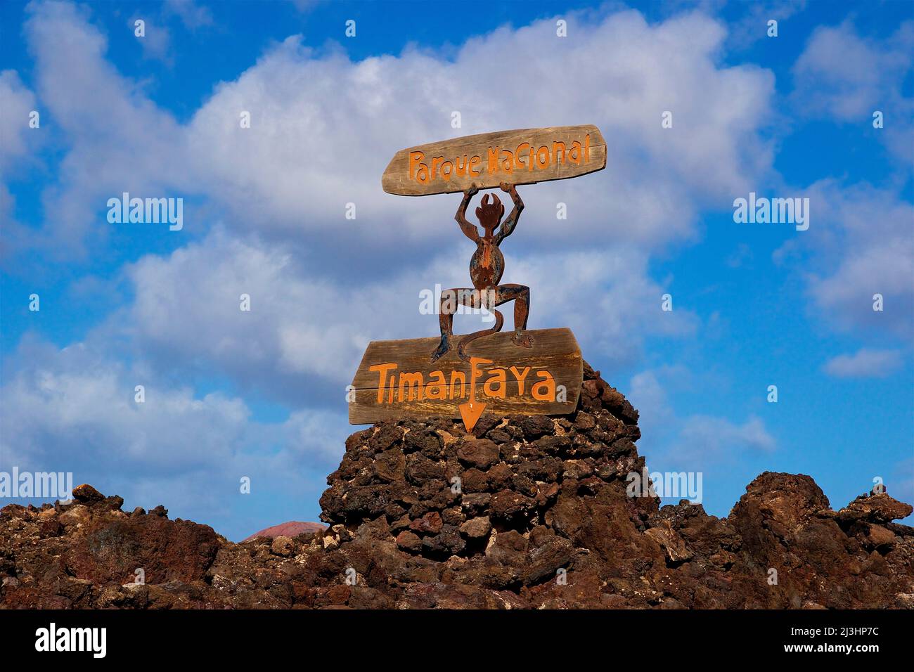Îles Canaries, Lanzarote, île volcanique, parc national de Timanfaya, paysages volcaniques, route d'entrée au parc national, panneau d'entrée en bois, figure du monument de Lanzarote, le diable de feu est sur le panneau 'Timanfaya', avec ses mains levées il tient le panneau avec l'inscription 'Parque Nacional ', ciel bleu avec des nuages blancs, la roche de lave se trouve autour du panneau Banque D'Images