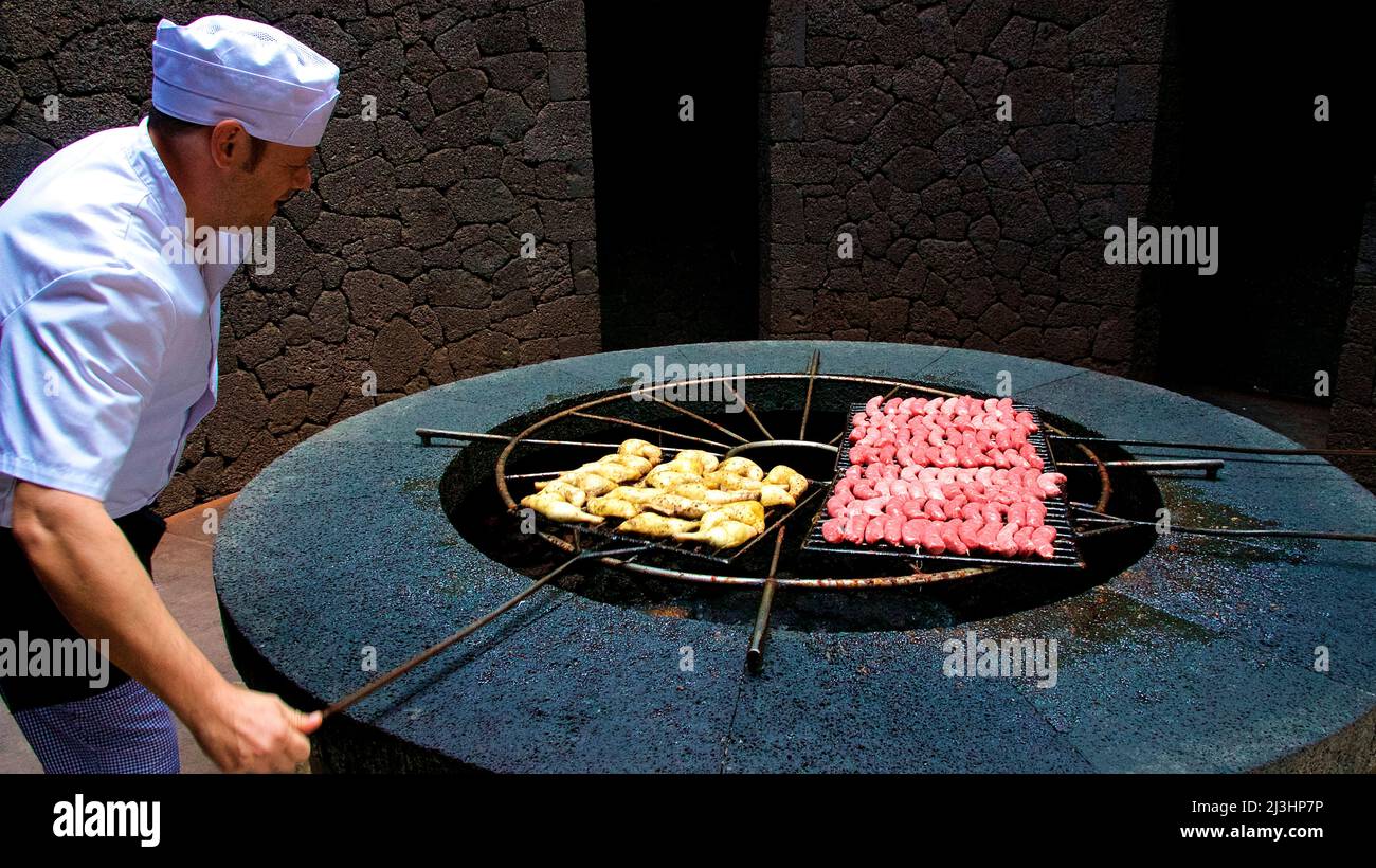 Îles Canaries, Lanzarote, île volcanique, parc national de Timanfaya, paysages volcaniques, gril alimenté par l'énergie géothermique, sur lui des saucisses et d'autres aliments grillés, à côté du gril tient un cuisinier dans les vêtements de travail blancs et avec un capuchon blanc et déplace la grille Banque D'Images