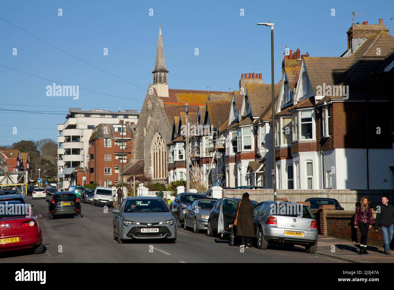 Bexhill-on-Sea, Sussex, rue résidentielle avec église, variété de logements, voitures et un couple Banque D'Images