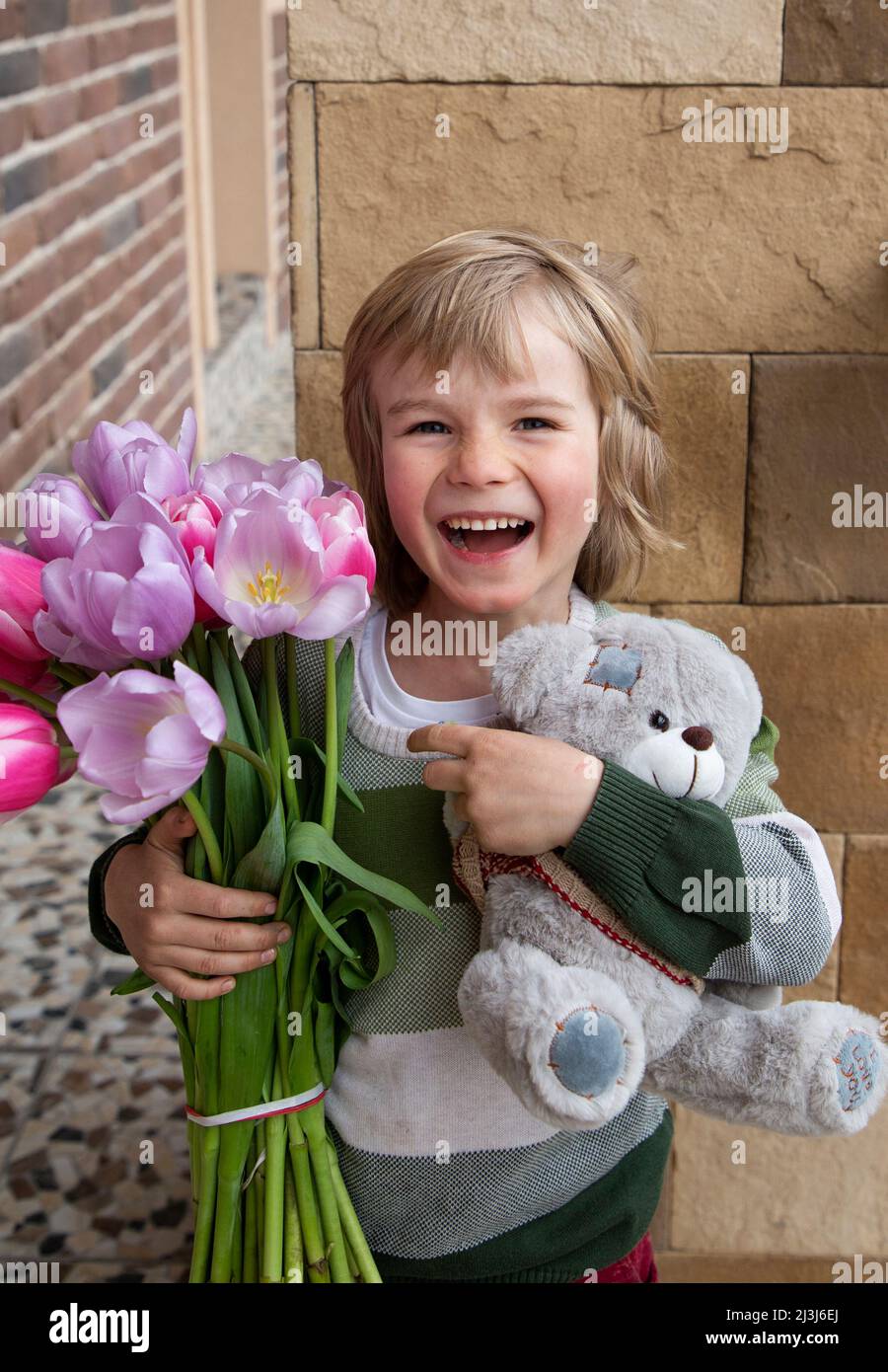 Joyeux garçon de 5-6 ans avec un bouquet de tulipes et un ours en peluche. Ambiance festive, un cadeau avec amour pour maman, grand-mère. Félicitations pour la da de mère Banque D'Images