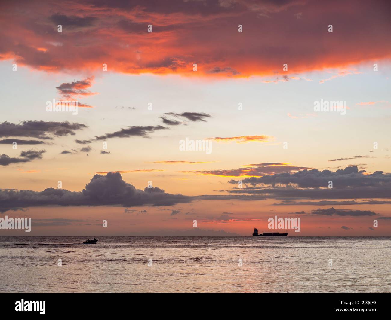 Magnifique coucher de soleil sur la plage avec ciel orange et bleu, vagues de l'océan et un bateau au loin. Banque D'Images
