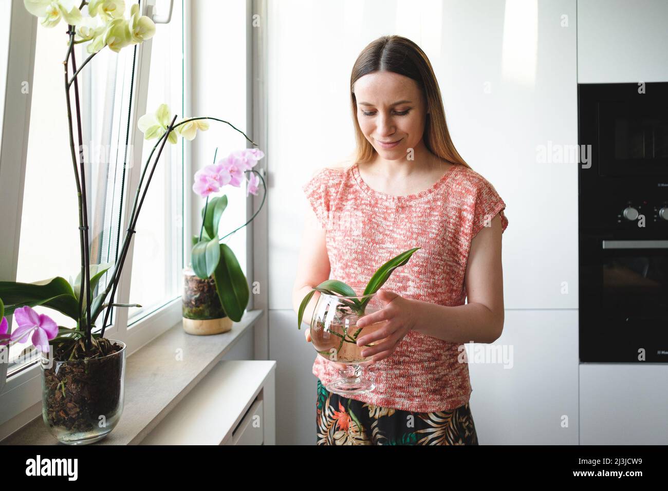 Une jeune femme authentique tenant une plante d'orchidée dans une can de verre avec de l'eau Banque D'Images