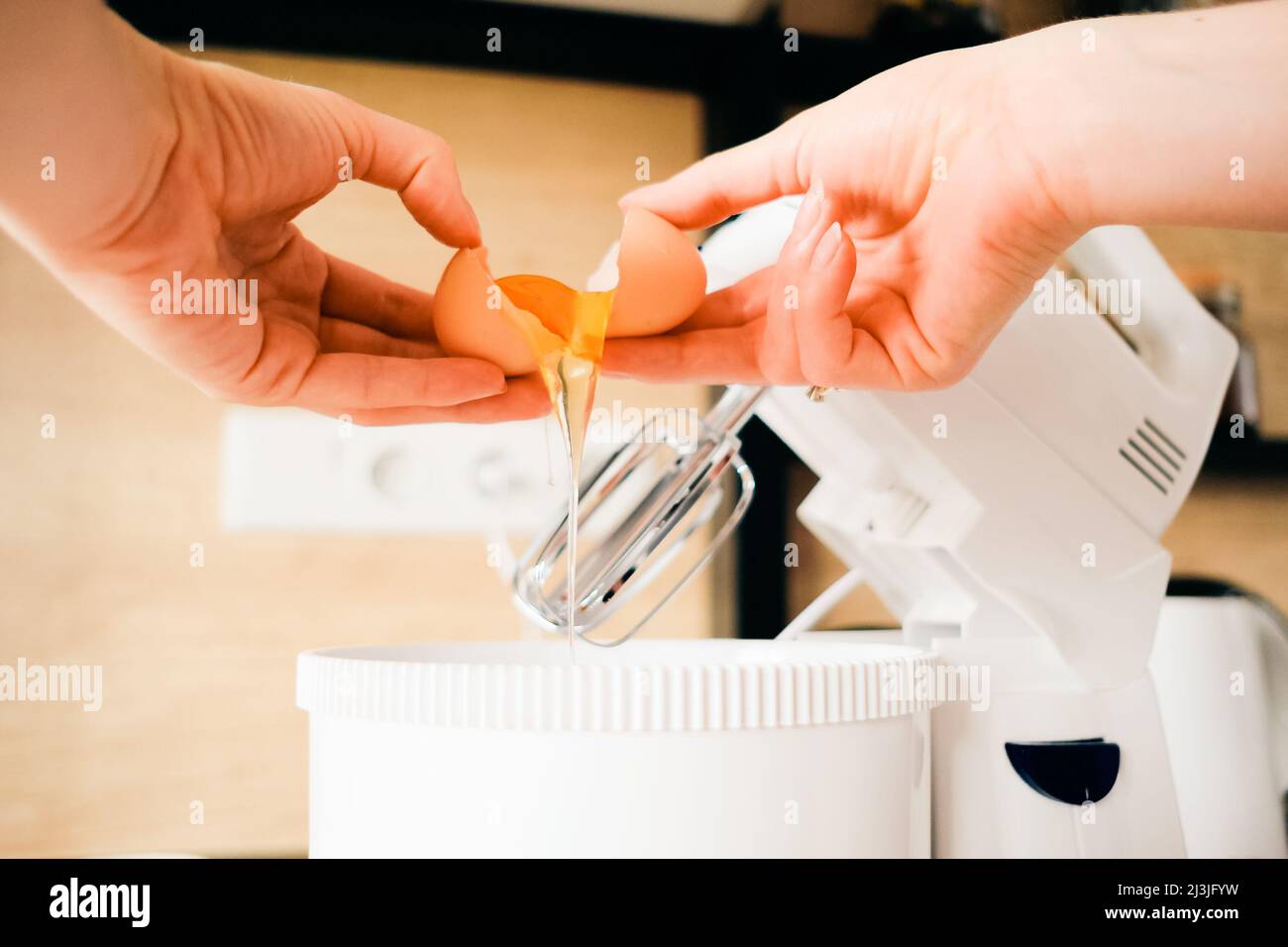 Gros plan femme mains casser des oeufs de poulet dans un bol mélangeur dans la cuisine. Pâte à cuire. Banque D'Images