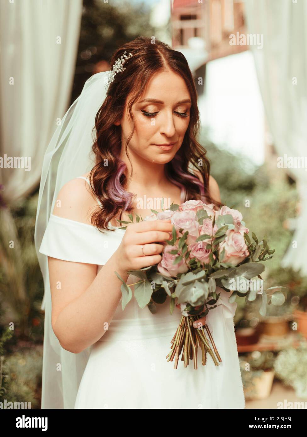 mariée dans une robe debout dans un jardin vert et tenant un bouquet de mariage de fleurs et de verdure grain effet Banque D'Images