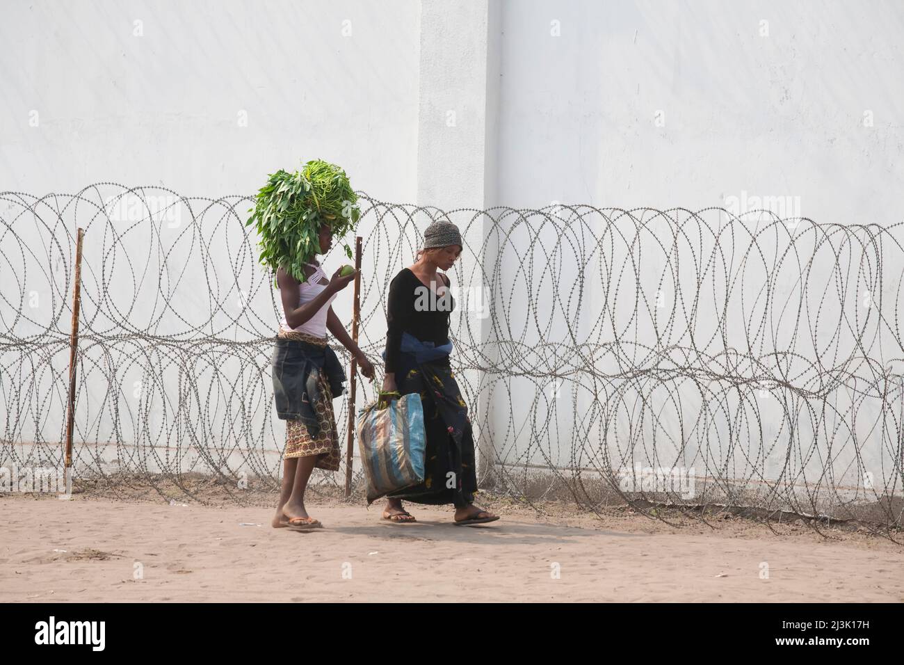 Les femmes congolaises marchent devant un fil de rasoir protégeant un bâtiment de l'ONU; Kinshasa, République démocratique du Congo. Banque D'Images
