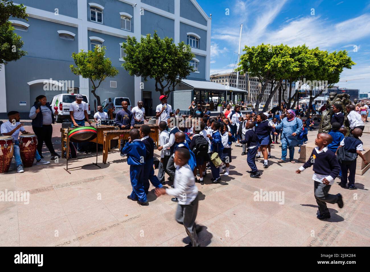 Les écoliers en uniforme s'arrêtent pour écouter un groupe musical de percussion le long du bord de mer du Cap, le Cap, en Afrique du Sud Banque D'Images