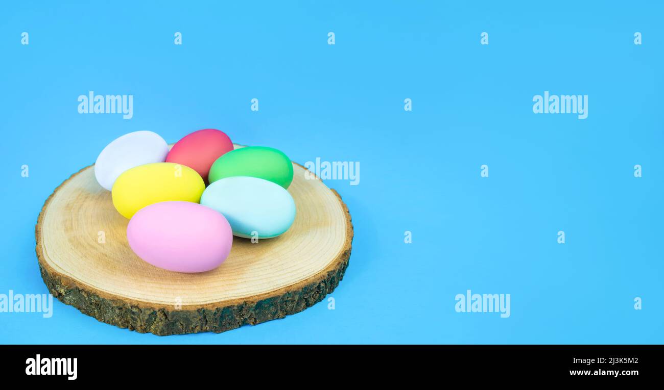 Oeufs de Pâques, simples, multicolores sur une assiette de chanvre sur fond bleu. Bannière Banque D'Images