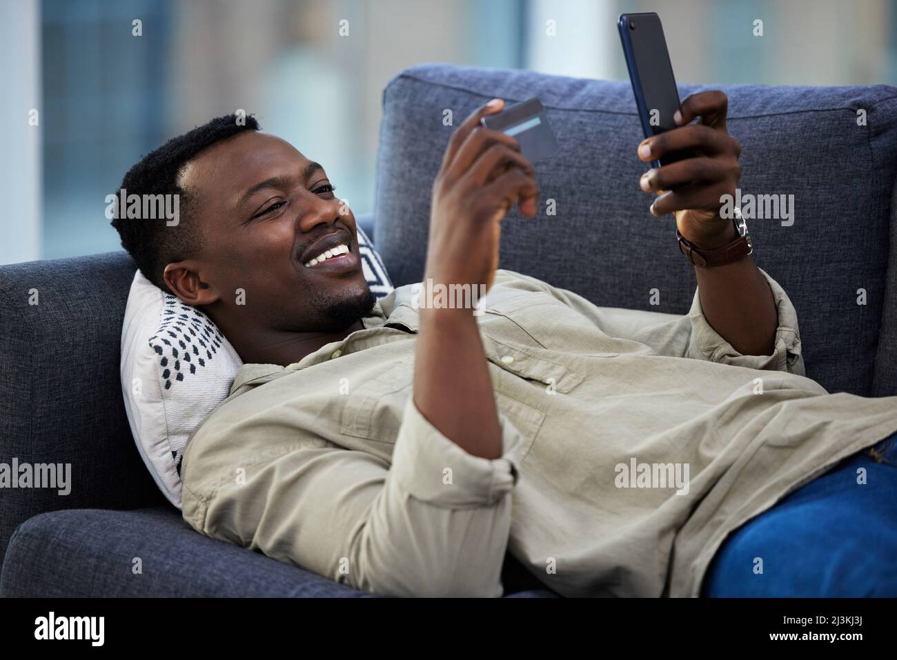 Faire du shopping dans le confort de mon canapé. Prise de vue d'un jeune homme à l'aide d'une carte de crédit et d'un téléphone sur le canapé à la maison. Banque D'Images