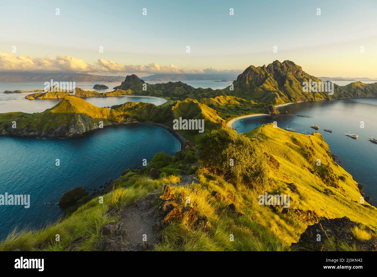 Des bateaux amarrés dans la baie de l'île de Padar dans le parc national de Komodo dans l'archipel de Komodo avec des pentes herbeuses ensoleillées au coucher du soleil Banque D'Images