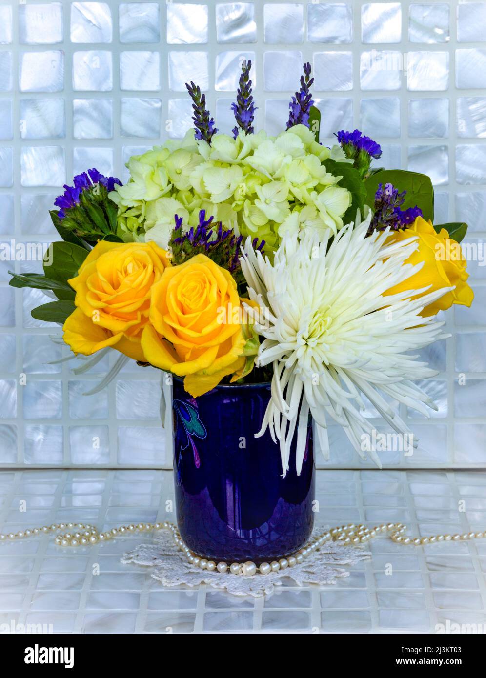 Bouquet de fleurs coupées fraîches dans un vase bleu avec un Doily crocheté et des perles, une variété de fleurs dans l'arrangement, y compris des roses jaunes et W... Banque D'Images