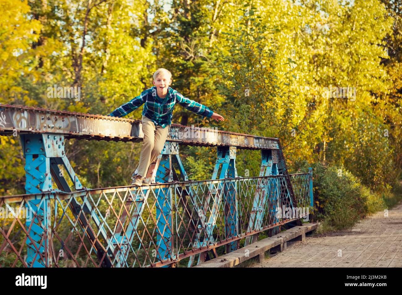 Garçon se tient sur une rampe de pont de parc, regardant avec le méfait vers la caméra; Edmonton, Alberta, Canada Banque D'Images