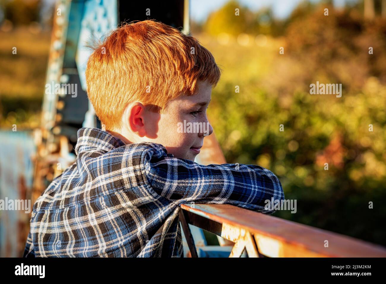 Portrait extérieur d'un garçon aux cheveux rouges debout sur un pont dans un parc donnant sur la rambarde; Edmonton, Alberta, Canada Banque D'Images