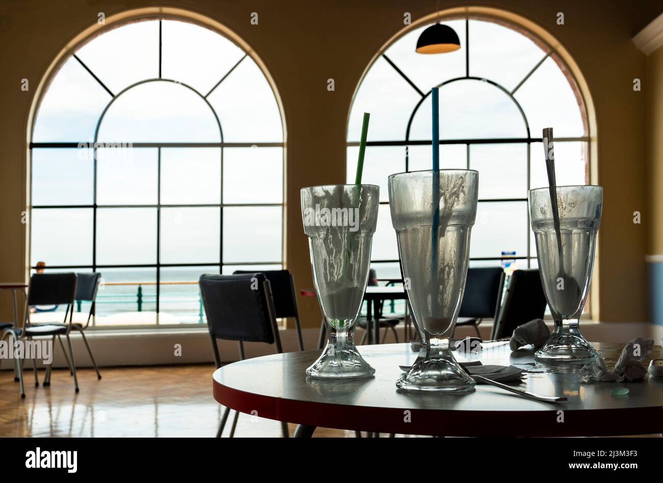 Videz les verres à milkshake sur une table de restaurant avec vue sur le front de mer et l'océan; Whitely Bay, Northumberland, Angleterre Banque D'Images