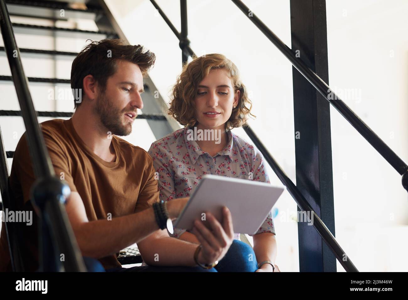 Qu'est-ce que nous pourrions modifier pour créer plus de valeur. Photo de deux concepteurs discutant de quelque chose sur une tablette tout en étant assis sur un escalier. Banque D'Images