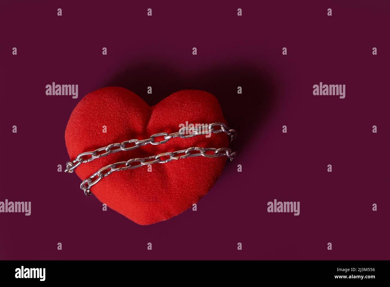 Dépendance d'amour. Un coeur jouet enroulé par une chaîne sur un fond coloré Banque D'Images