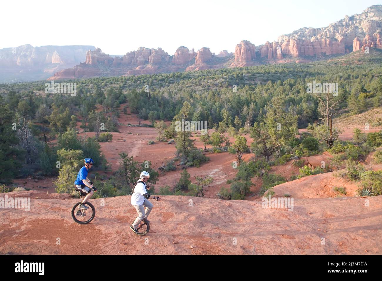 Deux hommes sur unicycles se promondent sur une crête rocheuse dans le désert de l'Arizona; Sedona, Arizona. Banque D'Images