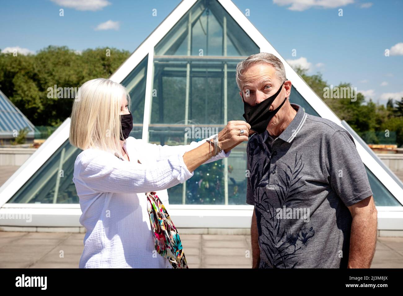 Un couple mature se tient dehors en portant son masque facial, la femme tirant le masque hors de son mari, pendant la pandémie Covid-19 Banque D'Images