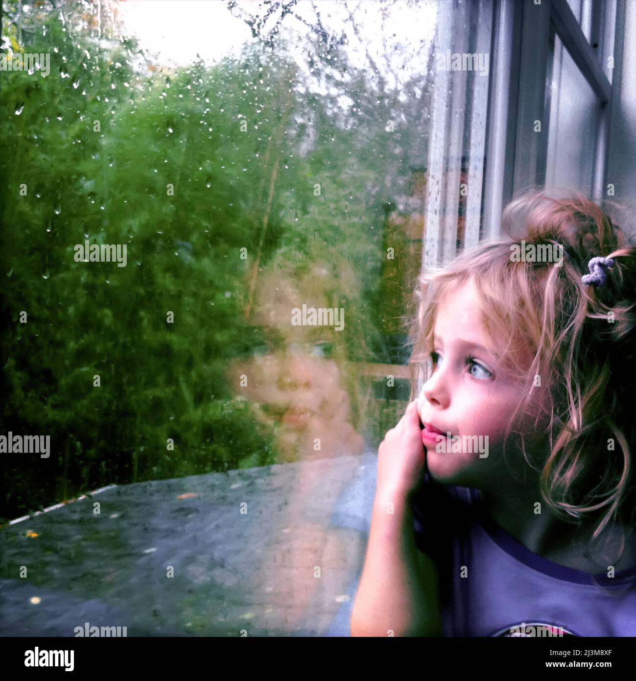 Une jolie fille de trois ans est près de la fenêtre par temps de pluie. ; Cabin John, Maryland. Banque D'Images