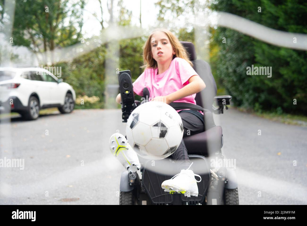 Une jeune fille de 11 ans atteinte de dystrophie musculaire congénitale d'Ullrich joue au football dans son fauteuil roulant près de sa maison Banque D'Images